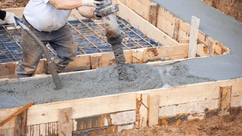 Pouring concrete into formed foundation footings over rebar and a vapor barrier